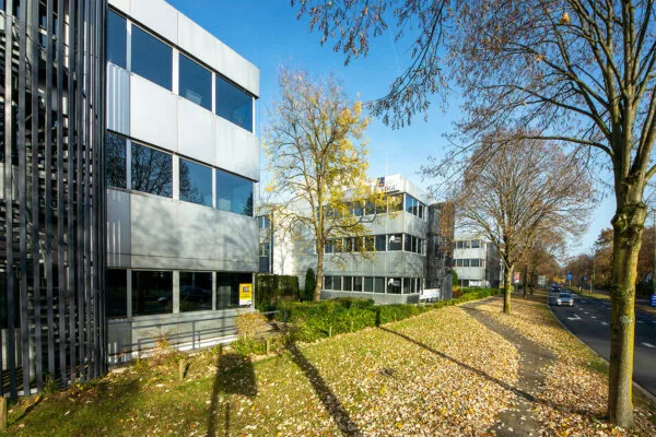 Kantoorgebouwen aan de Huis ter Heideweg in een herfstig straatbeeld met vallende bladeren en een blauwe lucht.
